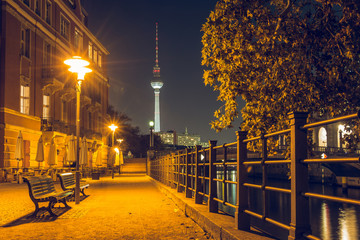 Fototapeta na wymiar Promenade on the Spree shore at night. Promenade near the museum island. In the background is the TV tower. There are benches on the way. The path is illuminated in autumn mood