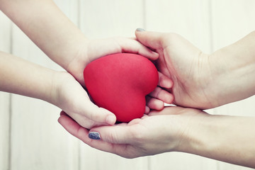 people, age, family, love and health care concept - close up of adult woman and young woman hands holding red heart over lights background. Female hands giving red heart