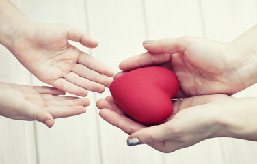 people, age, family, love and health care concept - close up of adult woman and young woman hands holding red heart over lights background. Female hands giving red heart
