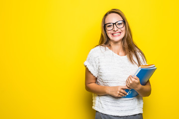 Cute woman writes some notes in notepad. Young student girl is thoughtful with pencil in hand and with backpack on yellow background