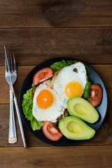 Avocado breakfast, fried eggs with whole grain toast bread on wooden background. Vertical image, top view.