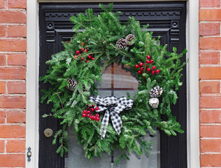 Fototapeta na wymiar front door of old brick house, with Christmas wreath made of pine branches and red berries