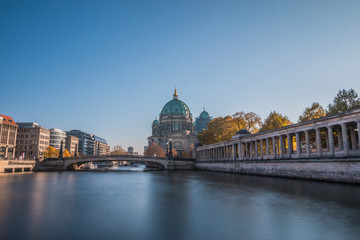 Fototapeta premium Berlin Cathedral with the Friedrich's Bridge at blue sky. Arcade of the National Gallery on the river bank of the river Spree with buildings of the capital Berlin