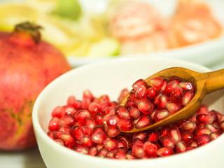 pomegranate seeds and wooden small spoon in white bowl.