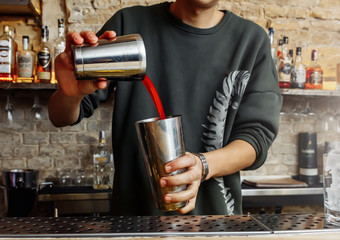 A barman with a shaker prepares a red cocktail.