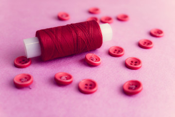 Beautiful texture with many round pink buttons for sewing, needlework and a coil of thread. Copy space. Flat lay. Pink, purple background