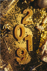 New Years Eve celebration background with champagn glass, 2019 number made with golden glitter candles, christmas decoration around, flatlay over a golden board, luxury  holiday concept