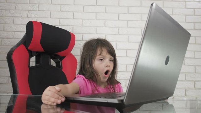 A child on the Internet. Child in shock looking at laptop. The little girl opened her mouth in surprise looking at the laptop screen. Children on the internet without parental supervision.