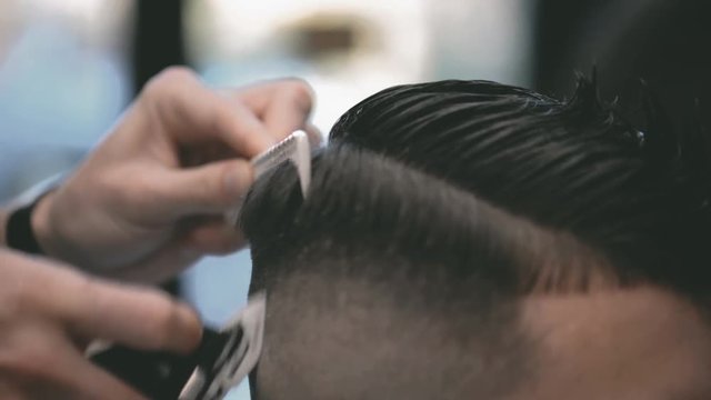 Close-up view on male's hairstyling in a barber shop with professional trimmer. Man's haircutting at hair salon with electric clipper. Grooming the hair.