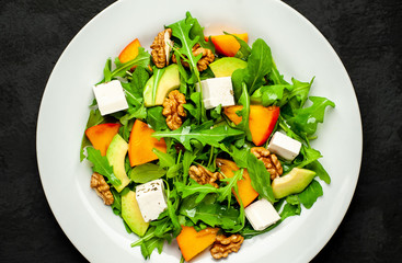 Avocado salad with baby spinach and pomegranate on a white plate on the background of slate, stone or concrete.