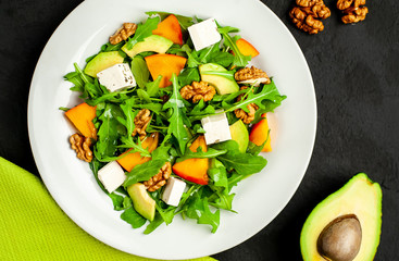 Avocado salad with baby spinach and pomegranate on a white plate on the background of slate, stone or concrete.