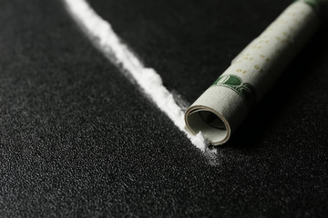 Line of cocaine and rolled money bill on dark background, closeup