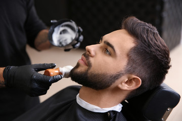 Professional hairdresser applying shaving foam onto client's skin in barbershop