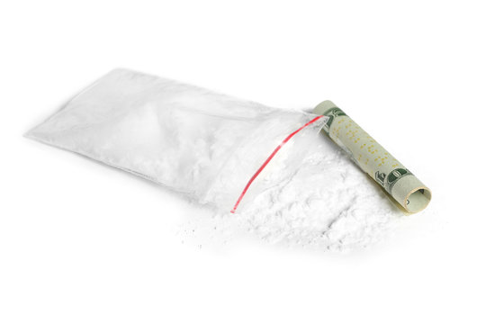 Cocaine in plastic bag and rolled money bill on white background