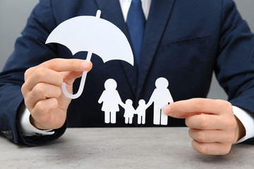 Fototapeta na wymiar Man holding cutout paper family and umbrella at table, closeup. Life insurance concept