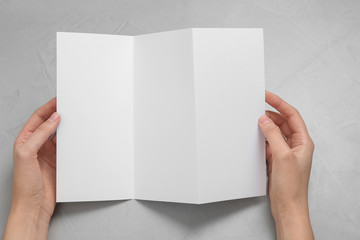 Obraz premium Woman with blank brochure on light background, above view. Mock up for design