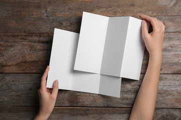 Obraz premium Woman with blank brochures on wooden background, above view. Mock up for design