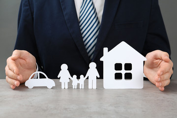 Man with cutout paper family, house and car at table, closeup. Life insurance concept