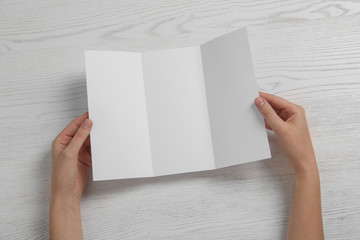 Woman with blank brochure on wooden background, above view. Mock up for design