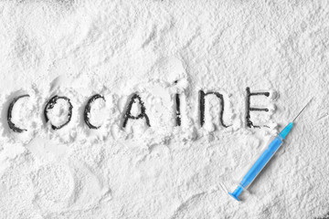 Syringe on white powder with written word Cocaine, top view