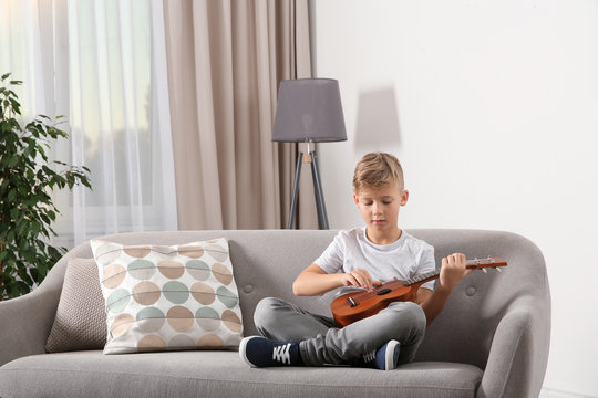 Little boy playing guitar on sofa in room. Space for text