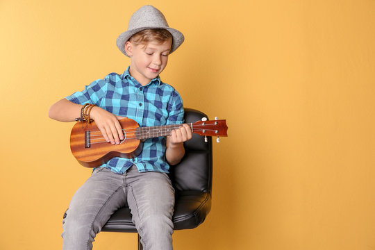 Little boy sitting on chair and playing guitar against color background. Space for text