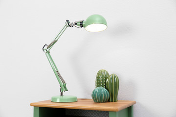 Stylish lamp and decorative cacti on table against white background