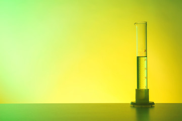 Graduated cylinder with liquid on table against color background. Chemistry laboratory glassware