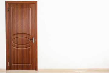 Closed brown door in white wall. Space for text