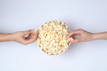 Women eating tasty popcorn from paper bucket on white background, top view