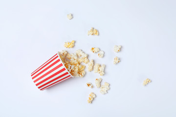 Overturned paper cup with tasty popcorn on white background, top view