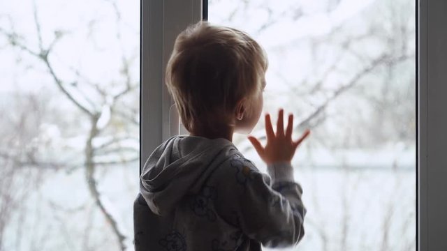 Child breathes on the window to be able to draw with finger on the window glass. Cold outside. 4K UHD Footage.