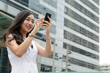 Beautiful woman playing mobile phone device and office building background.