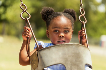 Cute little African American swinging at the park. - Powered by Adobe