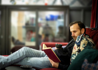 Obraz premium Young caucasian reading a book while sitting at sofa at home at night