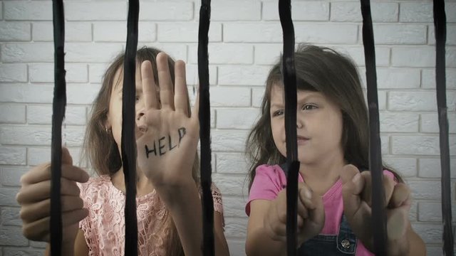 Sad children behind bars. Children in a cage. Sad little girls behind bars begging for help. Kidneping.