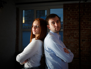 young couple back to back looking at the camera in the background loft interior window. The concept of a new home for a young family