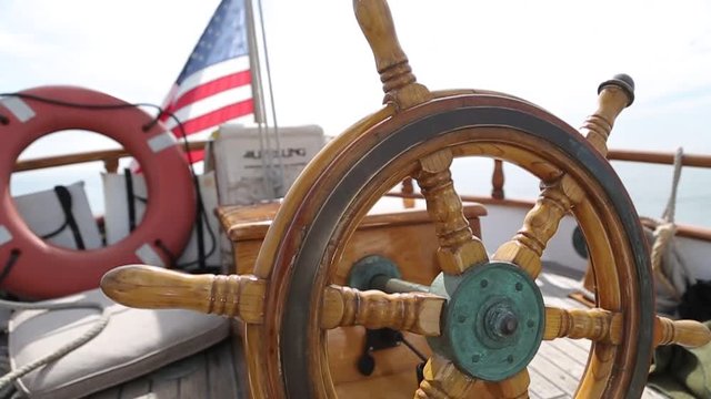 Closeup of a wheel and deck of a wooden antique sailing yacht rotating  steering wheel of Sail boat navigating in the ocean sunny day showing the wooden parts and accessories compass and detail aftern