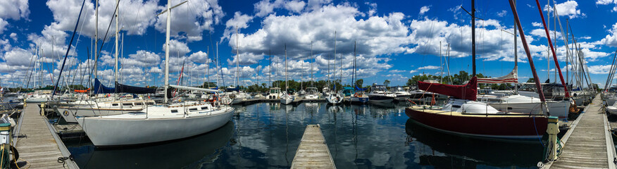 Fototapeta na wymiar Large sailboats tied up at dock in yacht club in summer with beautiful, blue cloudy sky, panorama