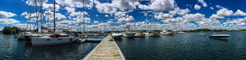 Fototapeta na wymiar Large sailboats tied up at dock in yacht club in summer with beautiful, blue cloudy sky, panorama