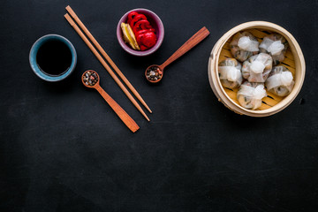 Chinese food set with dim sum, sticks and tea on black background top view copy space