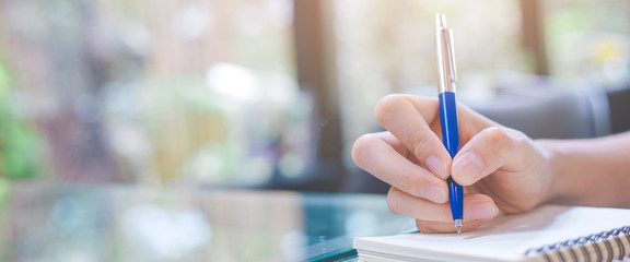 Woman writing on a notebook with a pen in the office.Web banner.