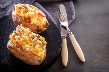 Baked potatoes with bacon and mushrooms in a rustic style in a black plate. Close-up. Copy space