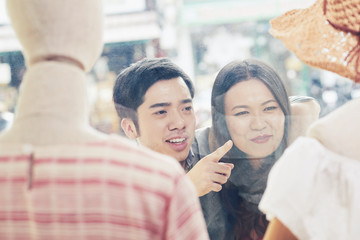 Obraz premium Young man looking at his girlfriend whe really wants a dress from shop window of fashion boutique