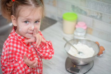 Cute caucasian little girl preparing the dough for pancakes or cookies from flour and eggs in the...