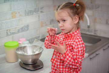 Cute caucasian little girl preparing the dough for pancakes or cookies from flour and eggs in the...