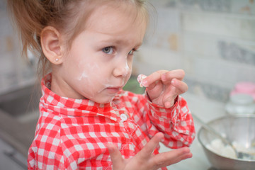 Cute caucasian little girl preparing the dough for pancakes or cookies from flour and eggs in the...