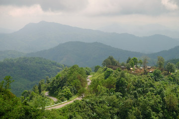 Road on green mountain to a countryside village at top of mount with background of multi layer...
