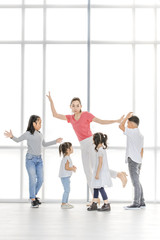 Asian woman in pink shirt teach Asian girls and boy do some body movement, they stand in front of big white window.