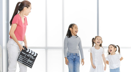 Asian woman in pink shirt Asian use clapper board in front of Asian boy and girls, they stand in front of big white window.